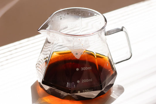 A minimal glass carafe of black coffee in warm sunlight